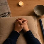 Méditation à domicile : mains en méditation sur coussin, bougie, carnet et plaid pour calmer le stress et mieux dormir